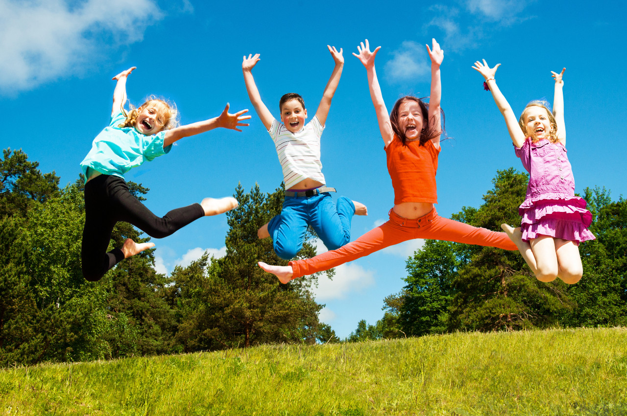 four kids jumping on grass